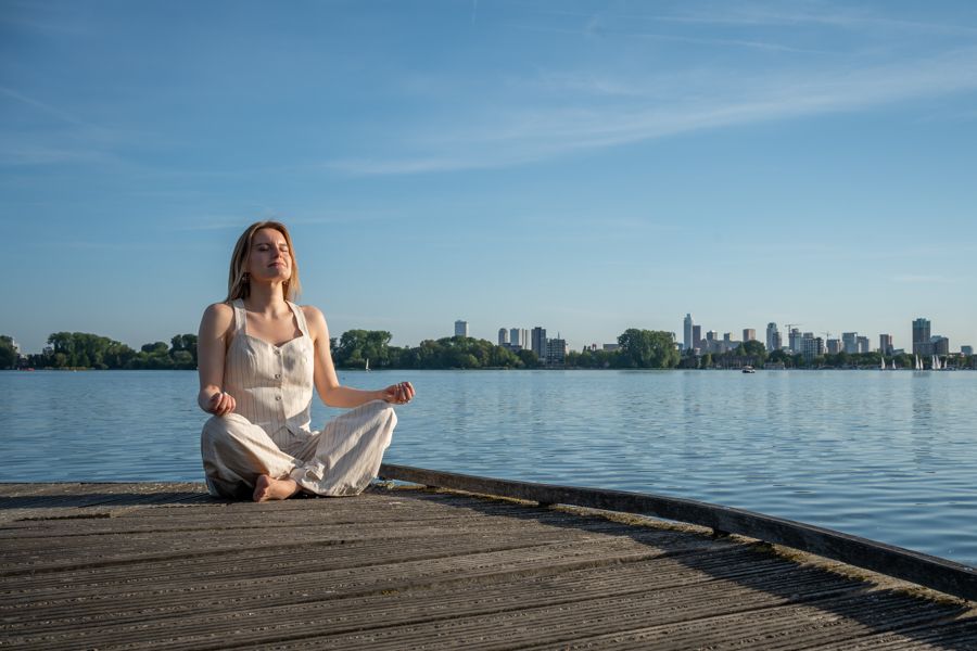 Gosia sitting cross-legged on a wooden pier by the water, eyes closed, breathing calmly