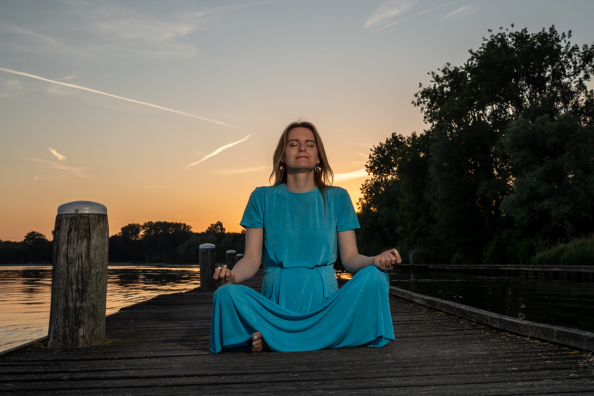 Woman sitting in meditation on a pier at sunset during a SOMA breathwork practice