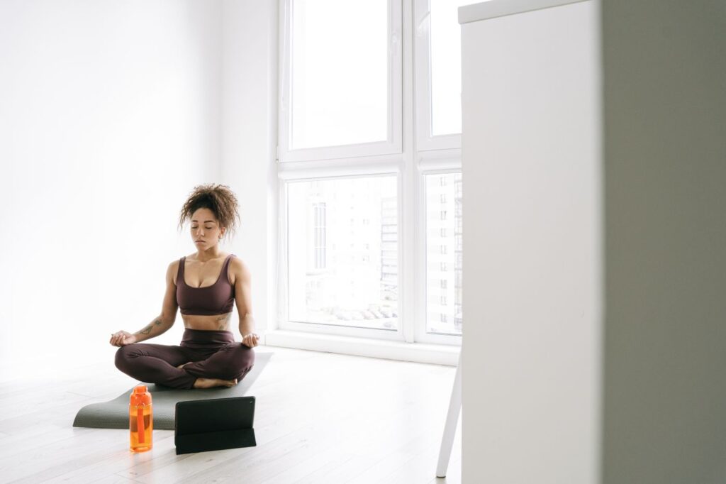 Woman sitting cross-legged by a bright window during a breathing practice at home