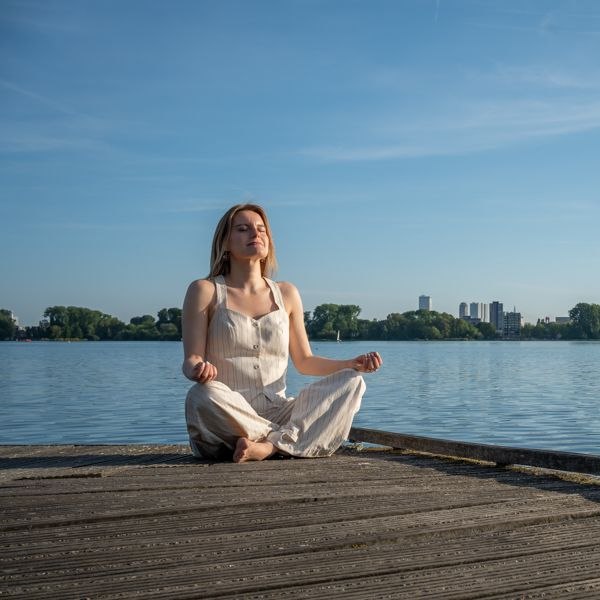 Gosia Sobczyk practising breathwork, seated with eyes closed on a pier by the river Maas in Rotterdam
