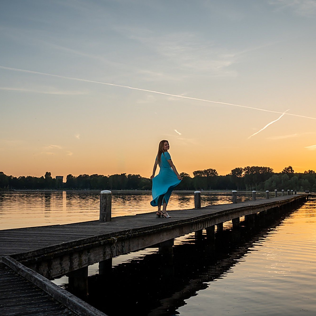 Gosia Sobczyk standing on a wooden pier at sunset in Rotterdam, wearing a flowing teal dress