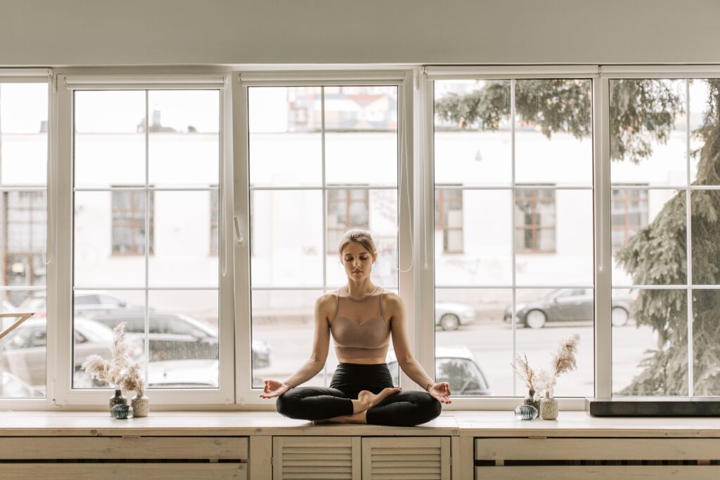 Woman sitting quietly in meditation by a bright window at home