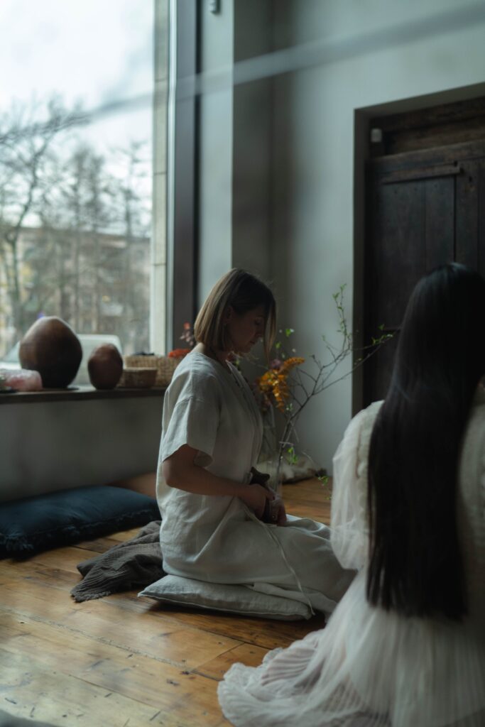 Two women practising meditation together by a bright window